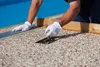 A person wearing white gloves is applying a textured material to a surface next to a blue pool. Produktbild-Vorschau