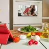 A kitchen scene with ingredients and a tablet, with a cooking video playing on an oven screen. Produktbild-Vorschau