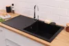 A black kitchen sink with a chrome faucet is installed in a wooden countertop, with a brick tile backsplash behind it. Produktbild-Vorschau