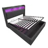 A dark gray upholstered bed frame with the mattress support lifted to reveal storage space underneath. The headboard has built-in shelves with purple LED lighting. Podgląd zdjęcia produktu