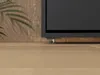 A close-up view of the bottom of a dark-colored cabinet bed frame with a wooden background and a wooden floor. Náhled obrázku produktu