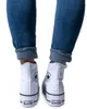 A person's legs wearing blue jeans and white Converse high-top sneakers. Voir les images du produit