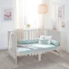 A baby crib with bedding and decorative pillows in a nursery setting. Produktbild-Vorschau