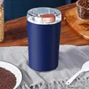 Dunkelblauer elektrischer Mühle mit durchsichtigem Deckel auf einer grauen Platzmatte, neben einem Teller mit gemahlenem Kaffee und einem weißen Löffel Náhľad obrázku produktu