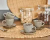 A collection of espresso cups and saucers are arranged on a woven placemat, with jars of sugar cubes and coffee beans in the background. Anteprima dell’immagine prodotto