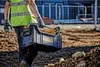 A construction worker carrying a tool box on a construction site. Podgląd zdjęcia produktu
