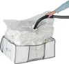 A hand is using a vacuum cleaner hose to remove air from a large, clear plastic storage bag filled with soft items. The bag is placed inside a grey and white fabric storage box. Produktbild-Vorschau