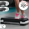 A person's legs and feet wearing leopard-print sneakers with pink laces are stepping on a black aerobic stepper in a gym setting. The stepper has white accents on the sides. There are inset images showing the stepper at different heights and a graphic indi Podgląd zdjęcia produktu