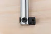 Close-up of a metal clamp with black rubber components on a wooden surface. Produktbild-Vorschau