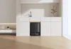 A black robot vacuum cleaner is docked in a modern kitchen cabinet. The scene is clean and minimalist, with white cabinets and wooden flooring. Produktbild-Vorschau