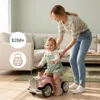 A mother is helping her child on a pink ride-on car in a living room. Produktbild-Vorschau