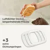 A hand holding a bamboo lid over a glass jar filled with coffee beans, with text overlay and a separate image of sealing rings. Produktbild-Vorschau