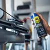 A hand is holding a can of RUNIX treadmill grease and spraying it onto a treadmill. Podgląd zdjęcia produktu