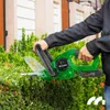 A person is using a green electric hedge trimmer to trim a bush. Podgląd zdjęcia produktu