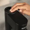A hand is pressing down on the top of a black water carbonator. Produktbild-Vorschau