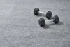 Two black dumbbells are placed on a gray carpeted surface. Produktbild-Vorschau