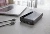 A power bank and cables are on a desk next to a laptop and a glass of water. Náhľad obrázku produktu