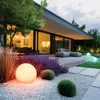 A modern house with a well-lit garden at dusk, featuring illuminated spherical garden lights. Podgląd zdjęcia produktu