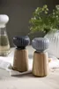 Two ceramic and wood salt and pepper grinders on a white cloth with a blurred background of greenery and a white vase. Podgląd zdjęcia produktu