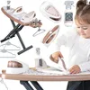 A young girl is playing with a toy ironing board and iron set, surrounded by various accessories. Produktbild-Vorschau