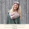 A woman wearing a scarf and sweater, standing in front of a wooden fence. Produktbild-Vorschau