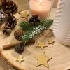 A festive Christmas arrangement on a wooden slice, featuring a lit candle, pinecones, fir branches, cinnamon sticks, and decorative gold stars. Produktbild-Vorschau