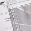 A close-up view of a grey sheer curtain with white stripes, attached to a white curtain rod with clips and strings. Text from a book or magazine is visible in the background. Produktbild-Vorschau