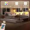 A bedroom scene featuring a white bed with a pull-out trundle, illuminated by LED lights. A remote control is shown in the foreground. Produktbild-Vorschau