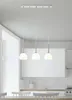 A modern kitchen with white cabinets and a tiled backsplash, featuring a three-light pendant chandelier hanging above a dining table. Produktbild-Vorschau