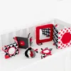 Several baby toys are arranged on a white surface, likely a crib or playpen. Produktbild-Vorschau