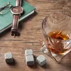 A whiskey set with stones, a glass of whiskey, a watch, and a book on a wooden table. Produktbild-Vorschau