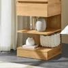 A close-up view of a wooden nightstand with shelves and a drawer, decorated with vases and books. Produktbild-Vorschau