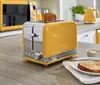 A yellow retro toaster with a slice of bread in it, sitting on a kitchen counter next to a microwave and kettle. Podgląd zdjęcia produktu