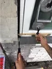 A person is using a tool to measure the gap between a window frame and a wall, with a folding ruler and a suction cup device visible. Produktbild-Vorschau