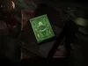 A green deck of cards with gold accents sits on top of two old books, with a candle and a glass object in the background. Náhled obrázku produktu