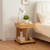 A bedside table with a lamp, plant, and books next to a bed. Podgląd zdjęcia produktu