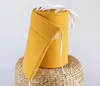 A rolled-up yellow baby crib bumper on a woven stool. Produktbild-Vorschau