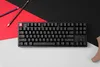 A black mechanical keyboard is placed on a surface with red and black paper behind it. Two pencils are also visible. Produktbild-Vorschau