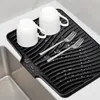 Two white mugs and two forks are placed on a black drying mat next to a sink. Produktbild-Vorschau