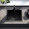 A black kitchen sink and faucet are shown from a top-down view, set against a grey stone countertop. Two small potted plants are visible on a white shelf in the background. Náhled obrázku produktu