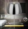 A close-up of a modern, chrome-finished LED table lamp with a touch control interface and a dimming slider shown in a blurred interior setting. Anteprima dell’immagine prodotto