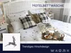 A neatly made bed with white bedding featuring a deer pattern, plaid pillows, and a tray with breakfast items. Produktbild-Vorschau