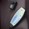 A close-up view of a massage chair remote control and its power adapter, resting on a brown leather-like surface. Náhled obrázku produktu