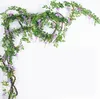 Künstliche Glyzinien-Girlande mit grünen Blättern und lila Blüten, drapiert über einem weißen Hintergrund Náhľad obrázku produktu