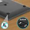 The underside of a black electronic device with rubber feet and a battery compartment is shown on a wooden surface. Produktbild-Vorschau