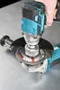 A hand is holding a power tool over another power tool with a cutting disc. Podgląd zdjęcia produktu