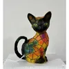 A colorful cat-shaped lamp sits on a white surface. Produktbild-Vorschau