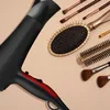 A collection of hair styling tools, including a hairdryer, brushes, and makeup brushes, laid out on a light beige background. Produktbild-Vorschau