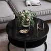 A round black coffee table with a floral arrangement, a small bowl of candies, and a candle holder, placed next to a gray sofa. Produktbild-Vorschau