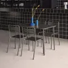 A metal table and four chairs set against a black tiled wall. Produktbild-Vorschau